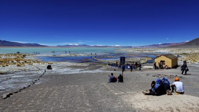 People enjoy the view of a desert landscape with a disused building and a lake, The Aguas Termales
