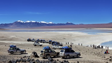 Several off-road vehicles parked in a desert landscape with mountains and snow-capped peaks under a