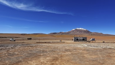 Vast, lonely desert landscape with a small building and snow-capped mountains in the background,