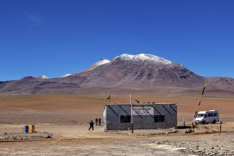 A small migration building in a vast desert landscape with snow-capped mountains, The border