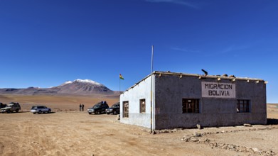 A small border building in a barren landscape with snow-capped mountains in the background, The