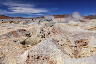Steam rises from craters in a vast geothermal desert landscape, the mud volcanoes and fumaroles on