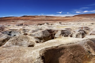 Vast, barren rocky landscape in the desert, two people on the horizon, blue sky, the mud volcanoes
