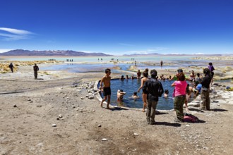 People enjoy a dip in a lake in the middle of a dry, barren desert landscape, The Aguas Termales de