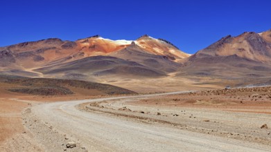 A sandy road winds its way through a vast, barren landscape under a bright blue sky, The landscape