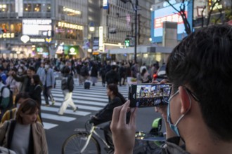 A tourist films the crowd at the zebra crossing of Shibuya Crossing with his smartphone,