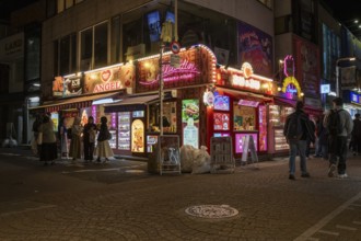 Tourists in front of a shop with illuminated advertisement for kebab and Japanese crepes in