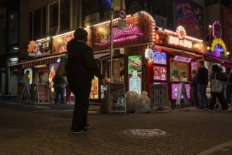 Tourists in front of a shop with illuminated advertisement for kebab and Japanese crepes in