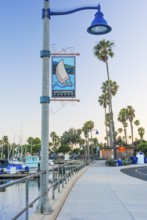A serene view of Santa Barbara Harbor at dusk, featuring a decorative street lamp with a banner, a