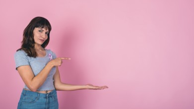 Young woman pointing and presenting with a pink ribbon for breast cancer awareness and copy space