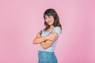 Young woman embracing herself with a pink breast cancer awareness ribbon on a pink backdrop