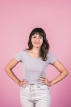 Young woman with hands on hips and copy space on pink background
