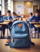 A blue backpack with orange accents sits on a desk in a classroom, with students focused on their