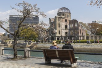 Tourists sitting on a bench under blossoming cherry trees, Sakura, Atomic Bomb Dome behind them,