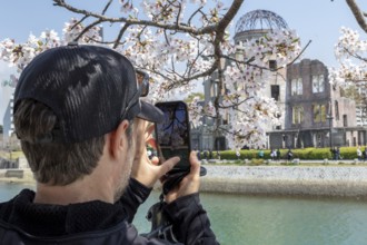 Tourist taking a photo of cherry blossoms with a smartphone, sakura, behind it atomic bomb dome,