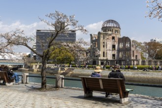 Tourists sitting on a bench under blossoming cherry trees, Sakura, Atomic Bomb Dome behind them,