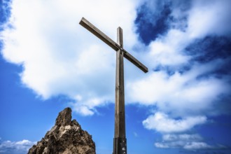 A wooden cross on a rock under a blue sky with white clouds. Kleinwalsertal Vorarlberg Austria
