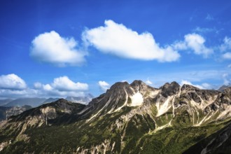 Majestic mountains under a clear blue sky with decorative clouds. Kleinwalsertal Vorarlberg Austria