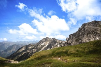 Green hills and rocky mountains under a clear blue sky with clouds. Kleinwalsertal Vorarlberg
