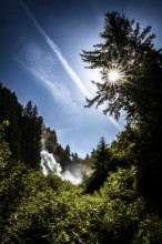 A waterfall in the forest under a bright sun and blue sky. Stuibenfall Austria Ötztal