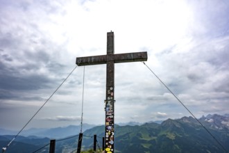 Large wooden cross on a mountain peak with a view of the surrounding Alpine peaks. Kleinwalsertal