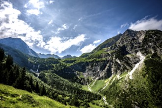 Sunny mountain scene with green slopes and dramatic clouds over the mountains. Kleinwalsertal