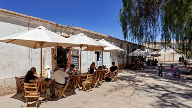 People sit in a café under parasols on the sunny street next to an old building, The town of San