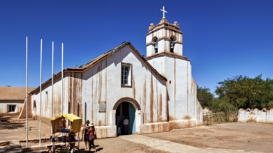 Church under a clear blue sky with people in the foreground and a cross on the tower, The church of