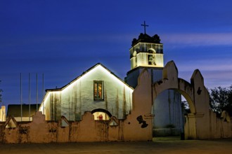 Church at dusk with illuminated tower and cross in front of a deep blue sky, The church of San