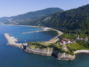 Coastal view with pier and green hills, surrounded by clear sea and scattered houses, aerial view,