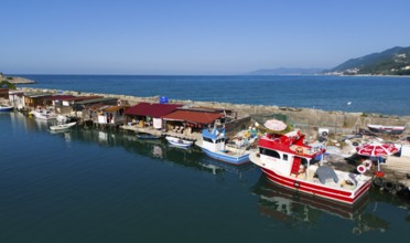 Fishing harbour with colourful boats and huts along a quiet coastline under a clear sky, aerial