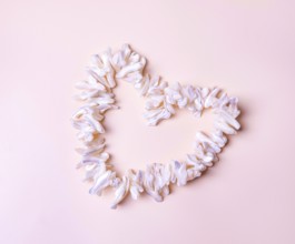 Heart made of mother-of-pearl white shells, on beige background, copy space