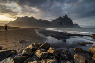 Two people standing on the beach, couple, adult, mountains, mountain range, sea, waves, surf,