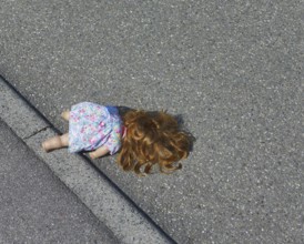 A doll lies on road surface in sunny ambiance