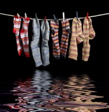 Clothesline with some multicolored sox fixed with clothes pins over reflective water surface in
