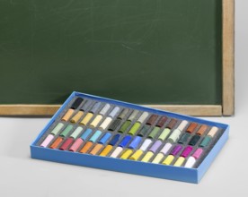 Edge of a old used blackboard and a box of crayons in front. Studio photography in light grey back