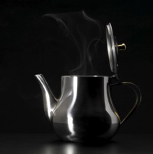 Studio photography of a steaming metal tea pot in dark back