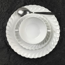 Studio photography of white porcelain plates and spoon on dark stone surface seen from above