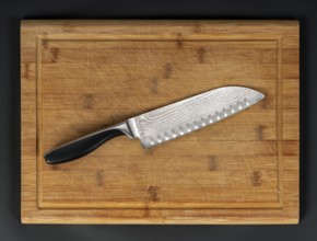 Pattern-welded knife on wooden bamboo cutting board in dark back