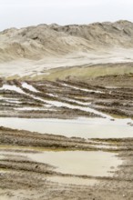 Wet scenery with skidmarks around a light brown heap of earth