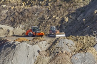 Roller compactor and bulldozer in stony hillside ambiance