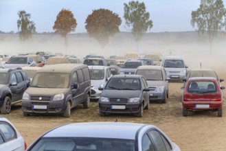 Dusty parking space scenery on a field including lots of dust covered cars at evening time in