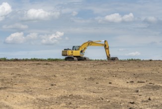 Yellow excavator at the horizon on earthen ground
