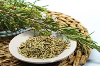 Fresh rosemary sprigs with flowers lie on a plate of dried rosemary, ready for culinary or