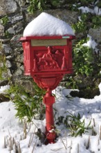 Vintage red mailbox under the snow, Ornate red mailbox covered in snow against a stone wall with
