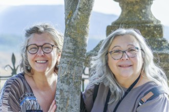 Two happy senior women enjoying a sunny day at the park, posing by a tree