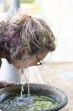 Woman refreshing herself by drinking water directly from a park fountain
