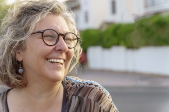 Portrait of a cheerful mature woman with glasses and nose ring laughing outdoors
