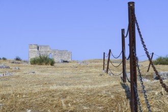 Rusty fence protecting an archeological site with ancient ruins under a clear blue sky, Malaga,