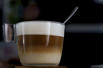 Latte macchiato in a glass cup with a spoon resting on the foam, showing the distinct layers of